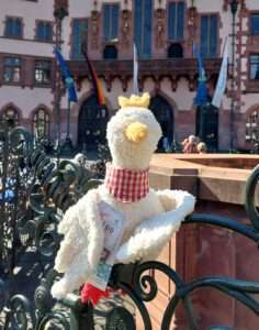 Ein Bilder Handpuppe Adler Fränki auf dem Geländer des Justitiabrunnen mit dem Römer im Hintergrund